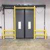 Yellow goal post style guardrail in front of gray swing doors