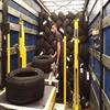 man inside a freight trailer with tires on a conveyor and a pile of tires behind him