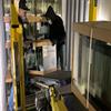 two men placing glass aquarium on conveyor in front of stack of aquariums inside freight trailer