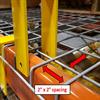 Two yellow prongs slotted into 2-inch by 2-inch openings in a wire deck on top of a pallet rack beam