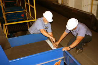 two men in hard hats working on a belted conveyor