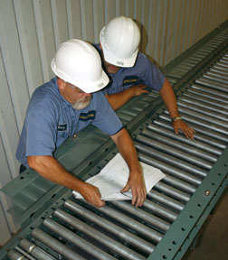 two men in hard hats consulting a document while working on a conveyor