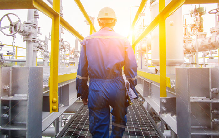 worker in a hard hat walking on a refinery walkway