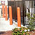 Orange bollards and plants surrounding an outdoor dining area with umbrellas