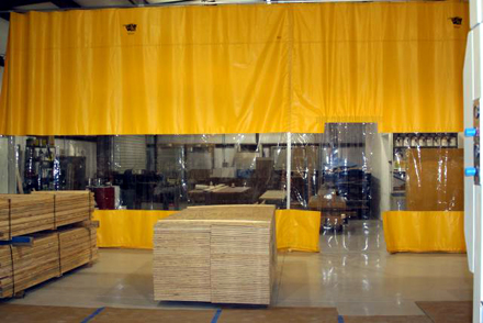 Yellow curtain wall with clear visibility panels separating lumber in a staging area