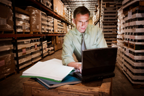 man working on laptop computer in warehouse with pallet racks